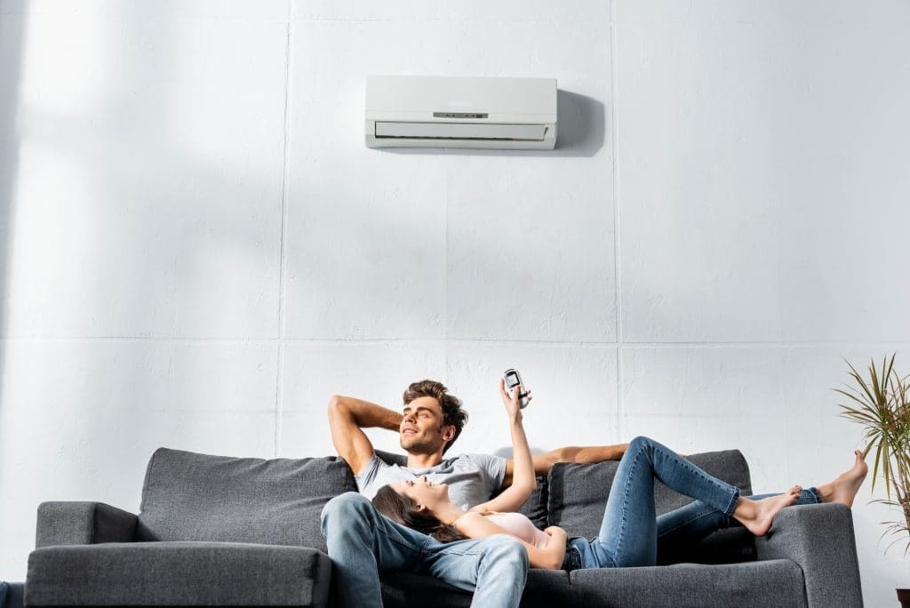 attractive girlfriend switching on air conditioner and lying on legs of handsome boyfriend